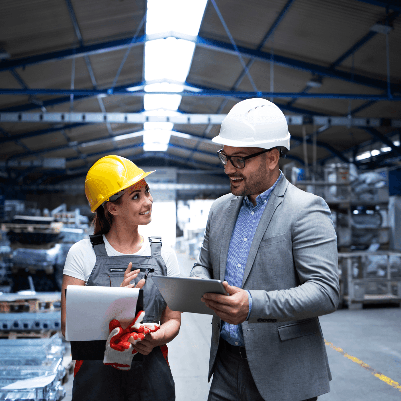 Male and female engineers in hard hats collaborating and reviewing documents on a tablet inside a manufacturing facility